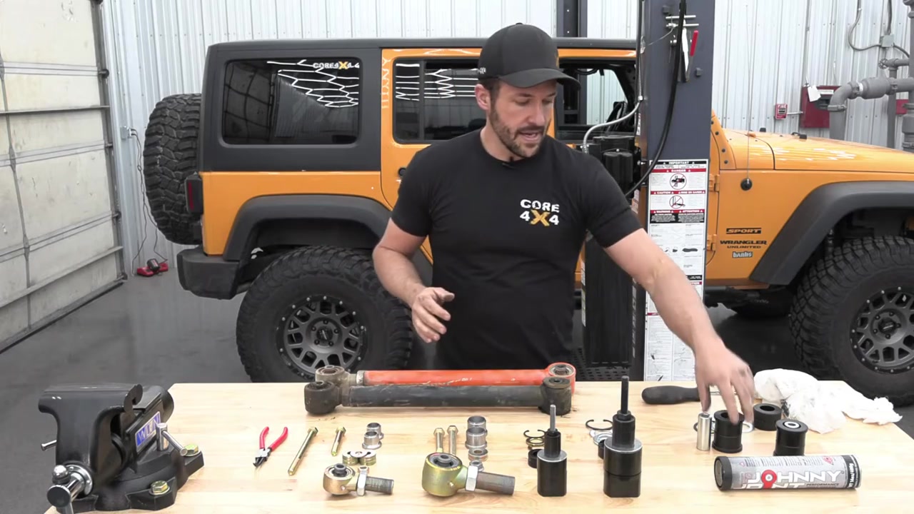 Control arm parts and rebuild tools laid out on workbench with orange Jeep JK in background