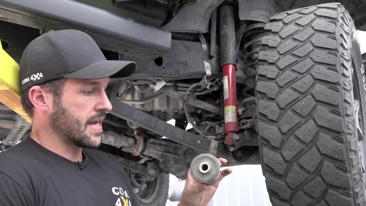 Spence holding a factory rubber control arm bushing under a lifted Jeep JL