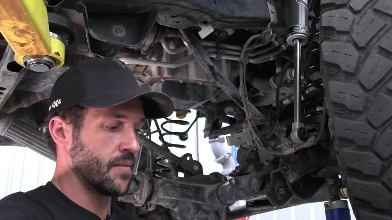 Installing front lower control arms under a lifted Jeep JL on the shop lift