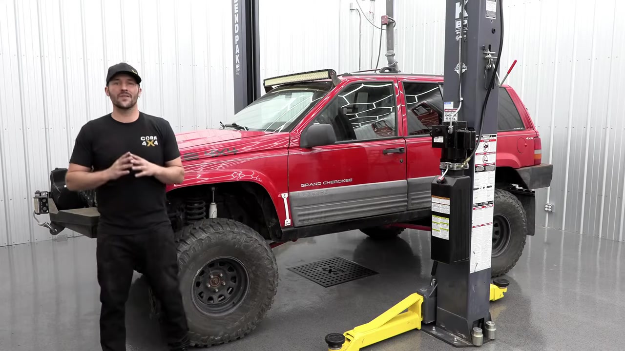 Spence from Core 4x4 standing next to a red ZJ Grand Cherokee on the lift before the long arm swap
