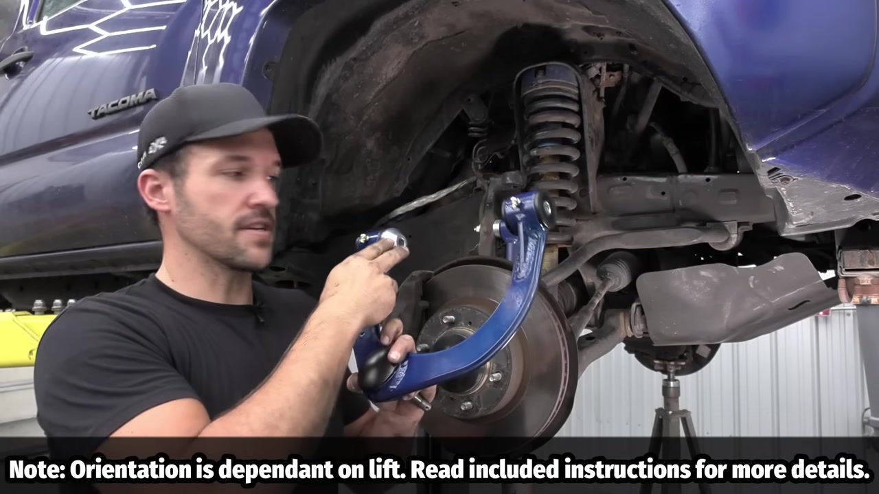CORE 4X4 upper control arm held up next to Toyota Tacoma wheel well showing spacer orientation for caster adjustment