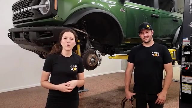 Spence and Marissa from Core 4x4 standing in front of a green 2022 Ford Bronco on a lift