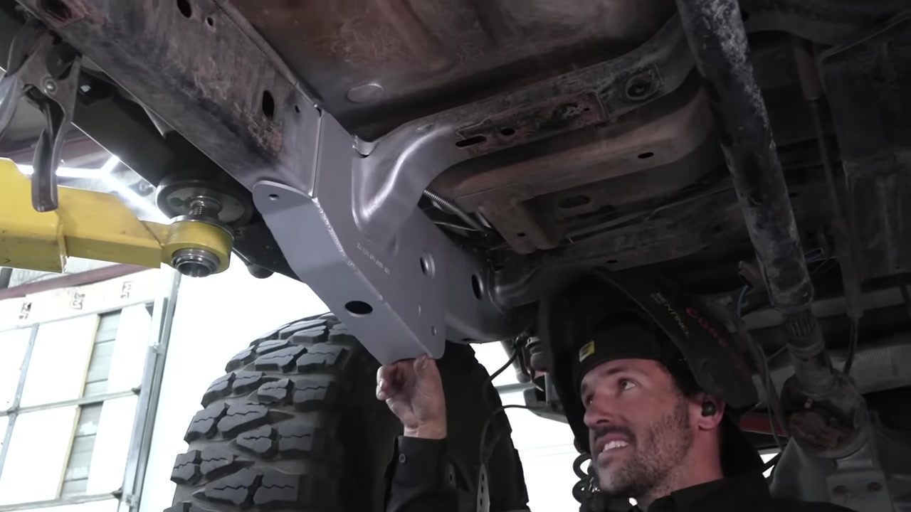 Spence positioning a weld-on long arm bracket against the JK Wrangler frame before welding