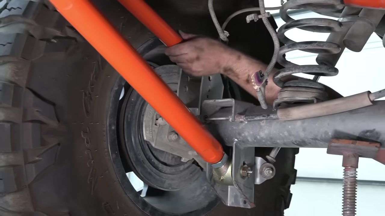 Close-up of the rear control arm being bolted to the axle bracket showing the orange arm and Johnny Joint hardware