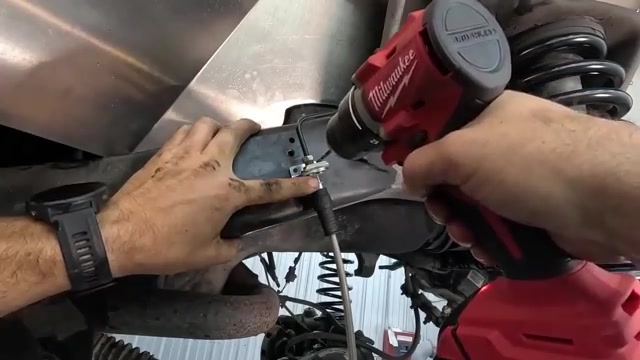 Close-up of control arm being bolted to the front axle with new coil spring visible on the LJ
