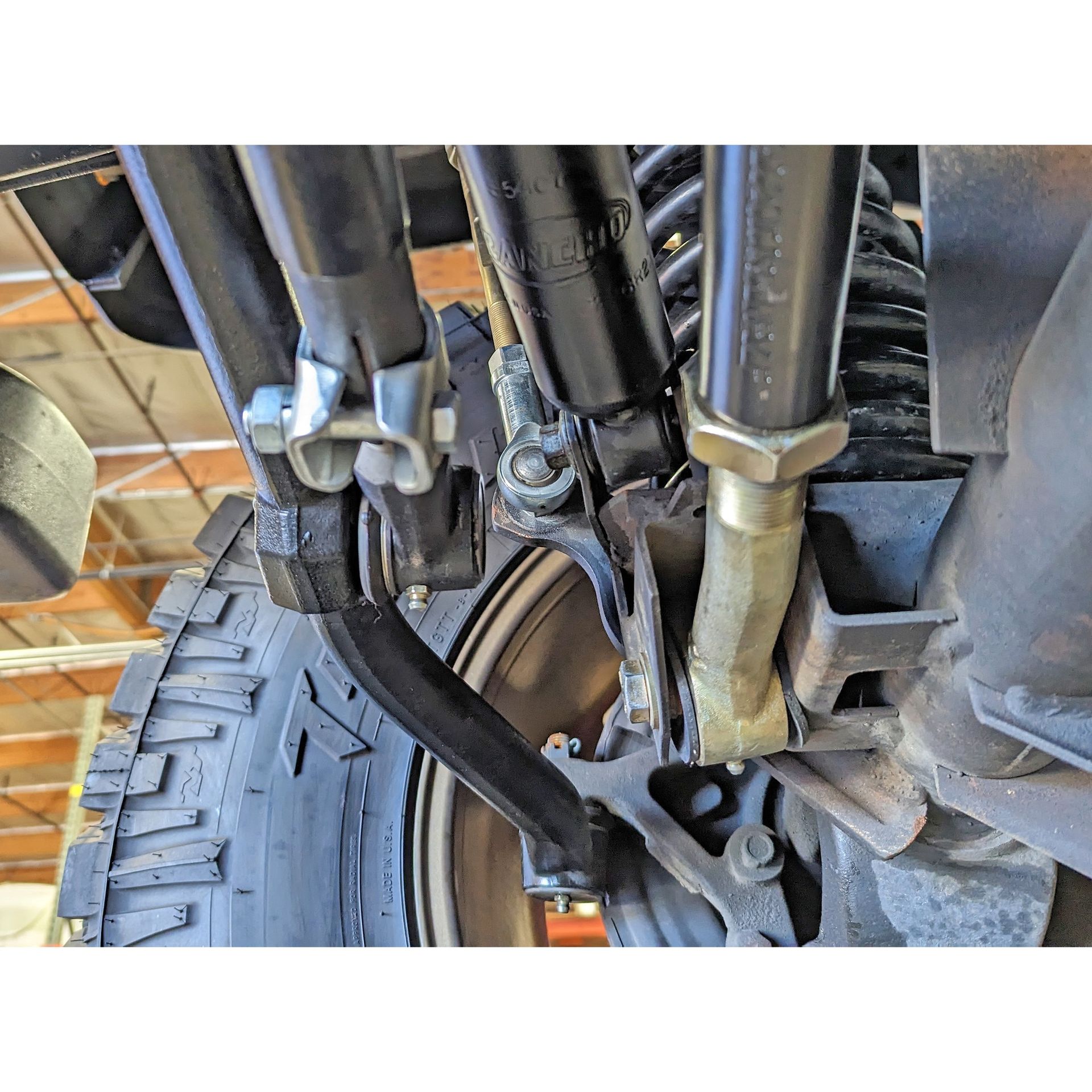 Full view of the installed RockJock Currectlync tie rod and drag link on the Jeep LJ front axle with coil spring and brake rotor visible