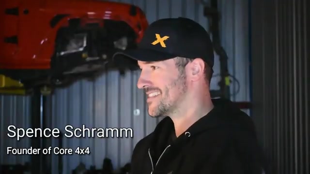 Spence Schramm, founder of Core 4x4, standing in the Core 4x4 shop with a Jeep on the lift behind him