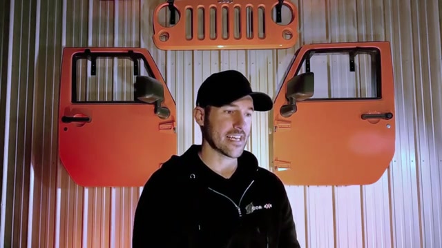 Spence Schramm, Core 4x4 founder, speaking in front of the iconic orange Jeep Wrangler doors and grille display in the Core 4x4 facility