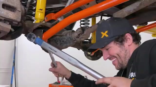 Core 4x4 team member installing orange adjustable control arms on a Jeep with a torque wrench, showing the hands-on quality of the build process