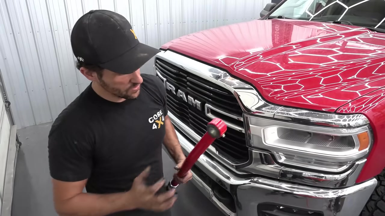 Spence holding the Core 4x4 adjustable track bar in front of the red Ram 2500 in the shop