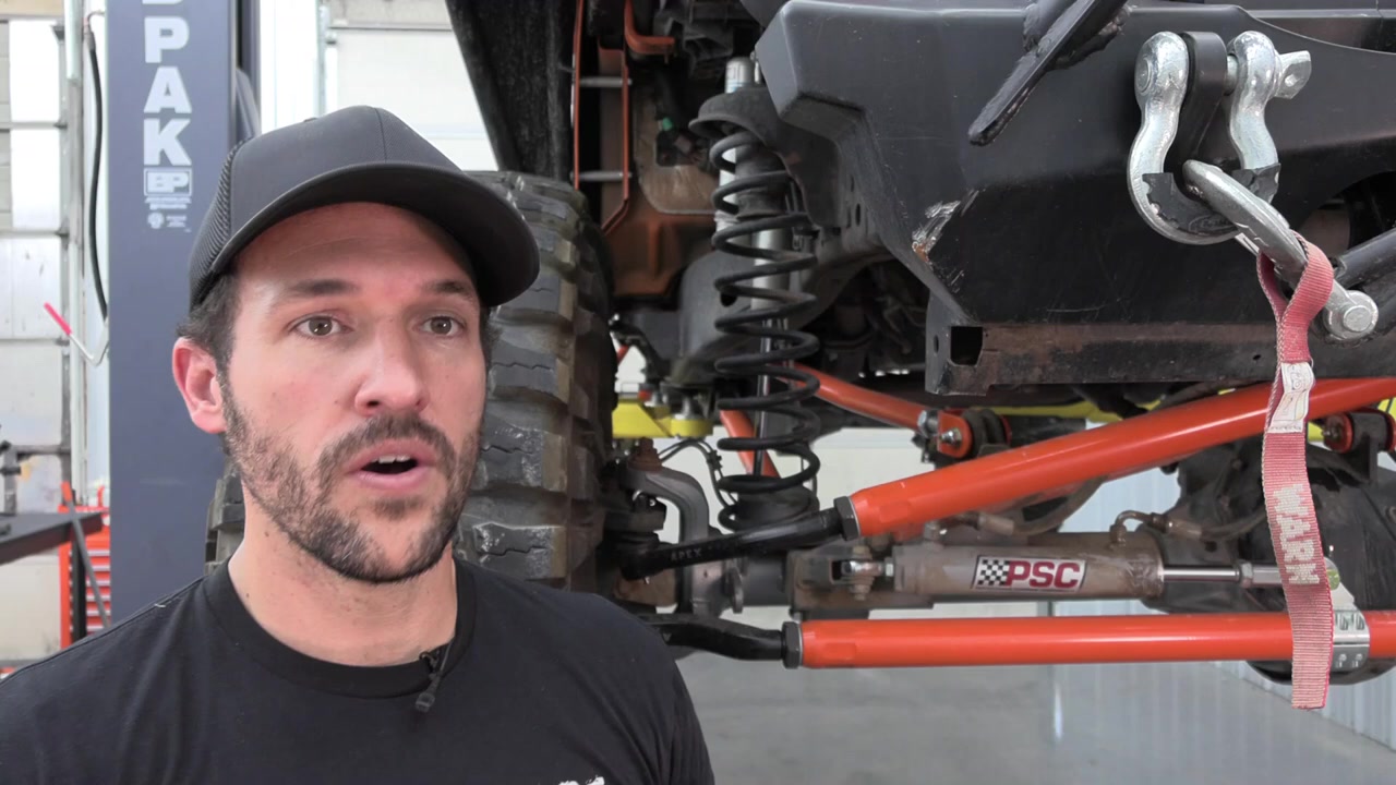 Spence standing next to the completed Jeep JK in the shop with bump stop extensions installed, showing the front suspension with new Core 4x4 control arms