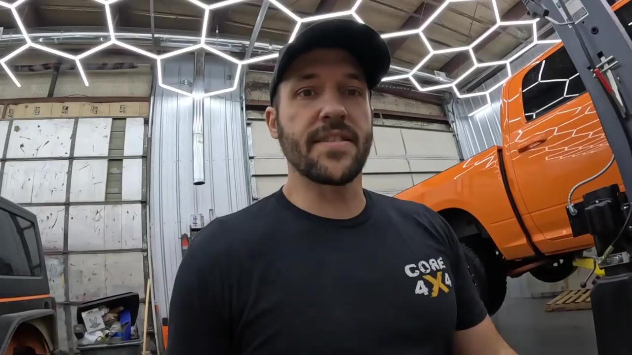 Core 4x4 host in the studio with the orange Ram 1500 on the lift ready for rear axle replacement