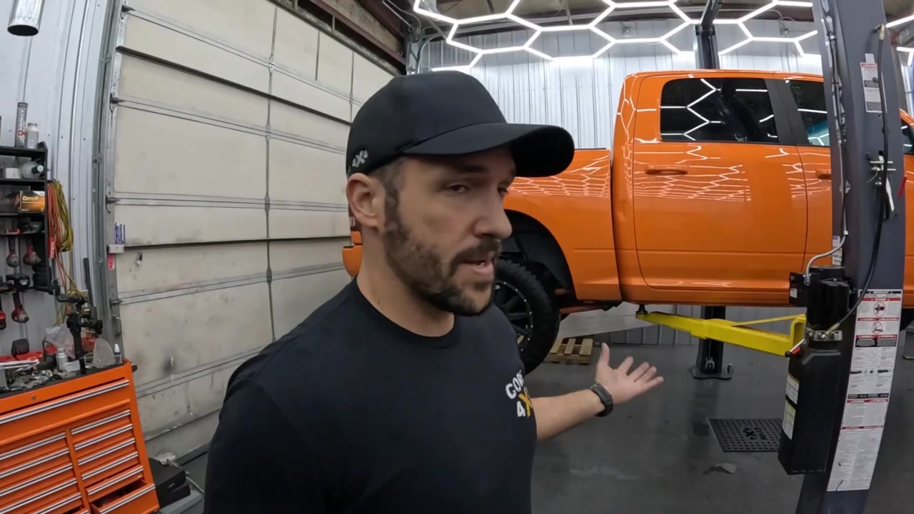 Core 4x4 host explaining the bent rear axle issue on the orange Ram 1500 on the lift