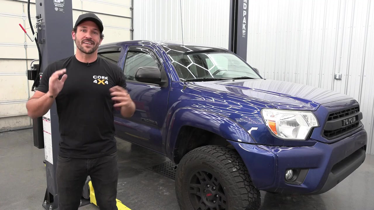 Spence from Core 4x4 standing next to a blue third-gen Toyota Tacoma in the shop before the front sway bar end link install