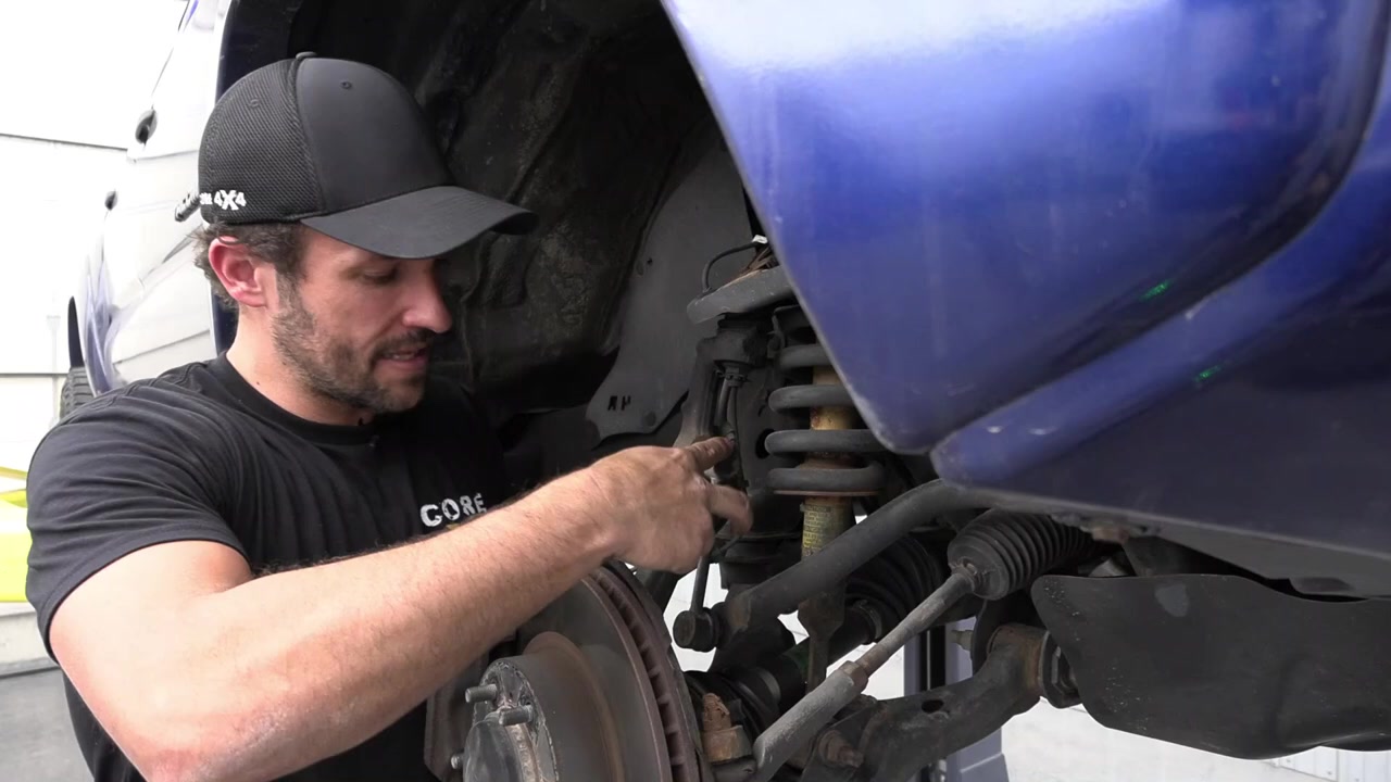 Spence working under the blue Tacoma examining the factory sway bar end link and suspension before removal