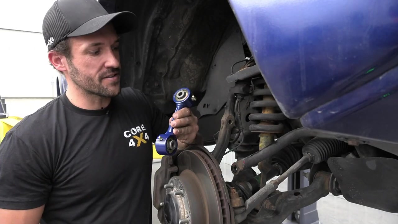 Spence holding the new Core 4x4 anodized blue sway bar end link next to the Tacoma front suspension before installation