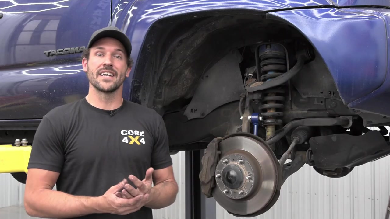 Spence standing next to the completed blue Tacoma with new Core 4x4 heavy duty sway bar end links installed, showing the finished front suspension