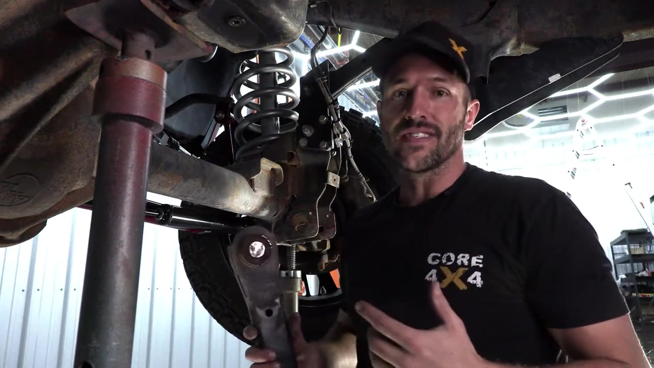 Spence under the Ram 3500 explaining the control arm removal process with the axle supported on jack stands