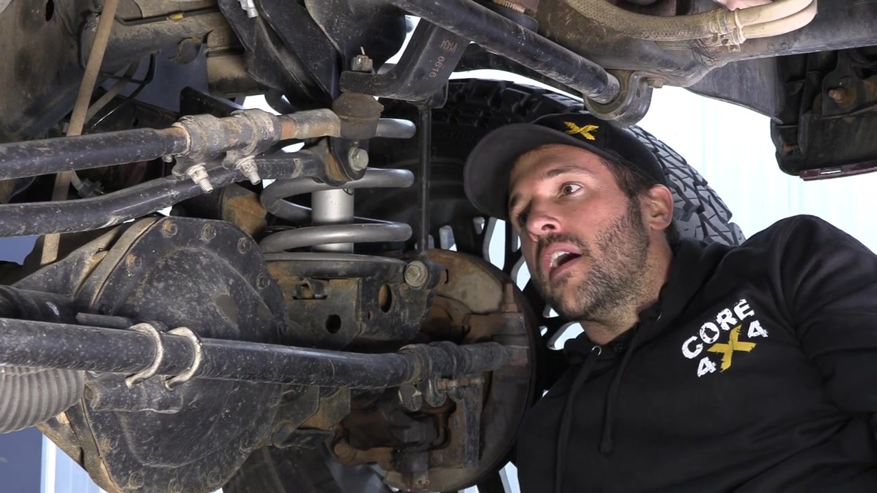 Spence under the Ram 3500 pointing out the factory track bar mounting location on the front axle