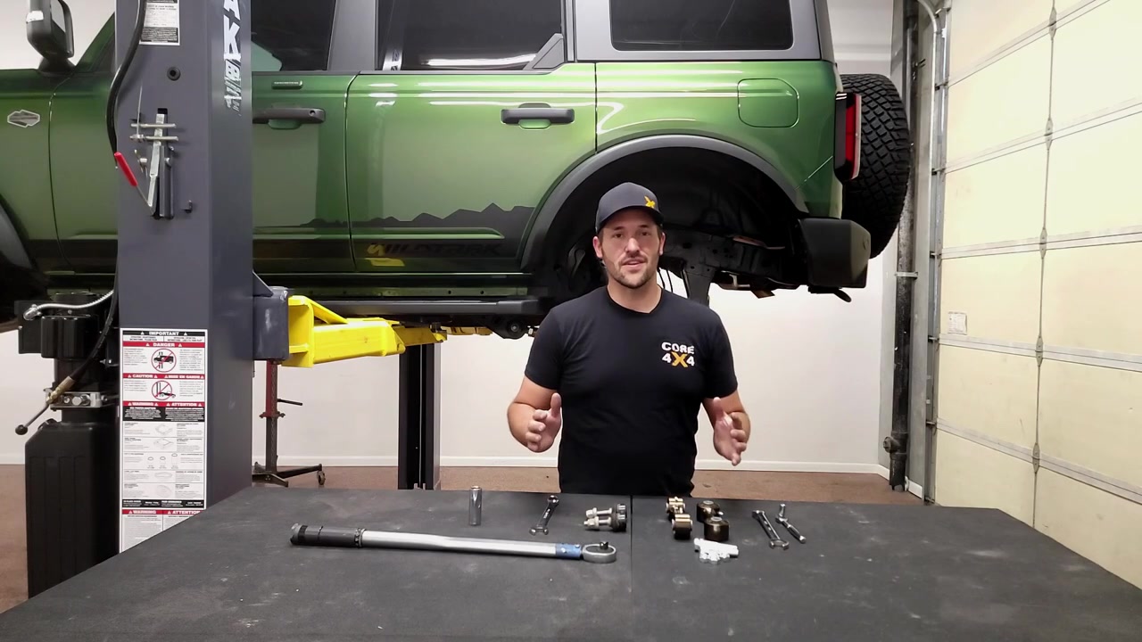 Spence from Core 4x4 standing in front of a green 2022 Ford Bronco on the lift with Crawl Series rear sway bar end links and tools laid out on the workbench