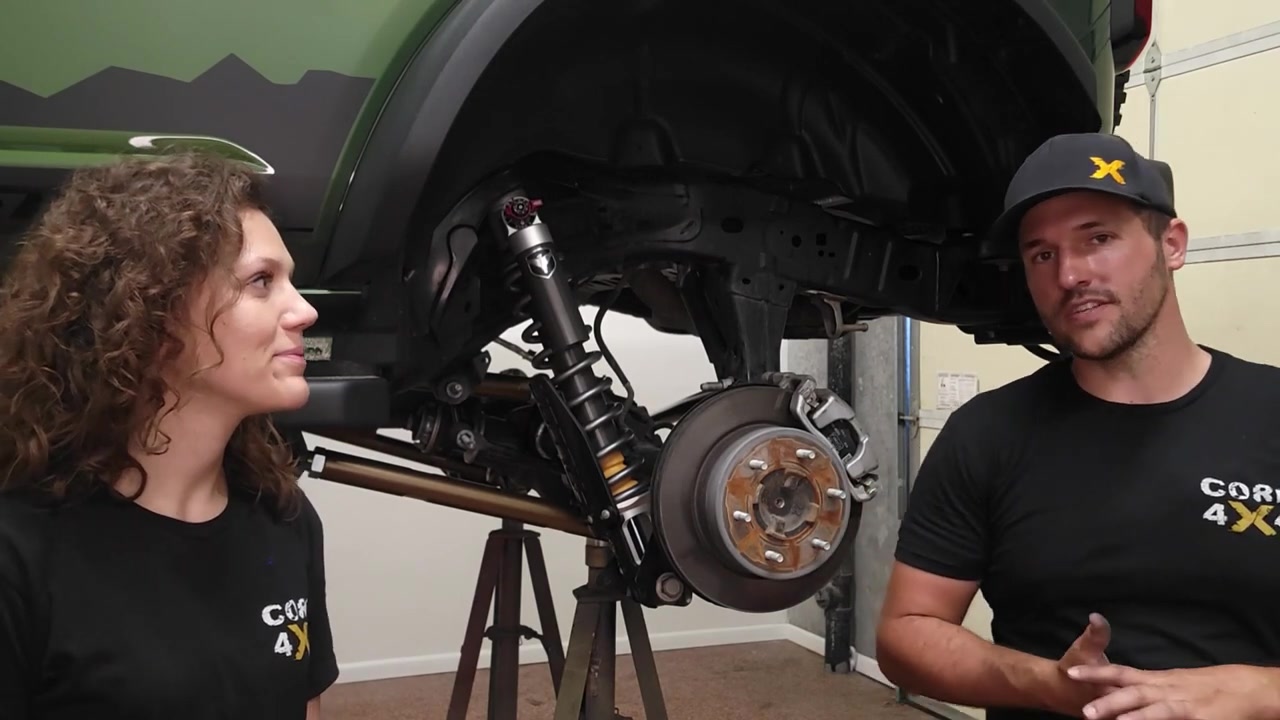 Spence and Marissa from Core 4x4 standing in front of the green Ford Bronco on the lift with new Falcon coilover and bronze control arms visible behind them