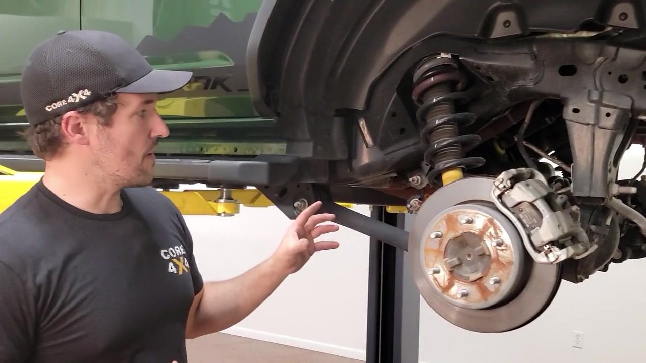 Spence pointing at factory rear suspension components on the 2022 Ford Bronco up on the lift