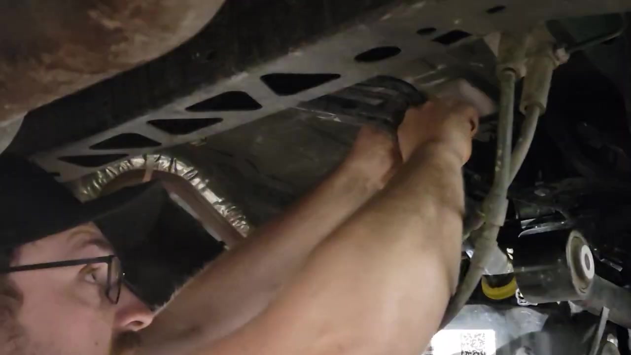 Trevor working underneath the Bronco to lower the gas tank using a transmission jack for access to the upper control arm bolt
