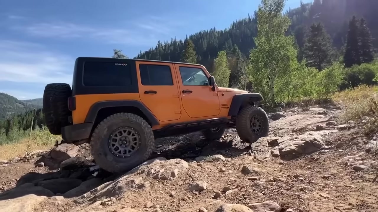 Orange Jeep Wrangler equipped with Core 4x4 suspension navigating a rocky mountain trail