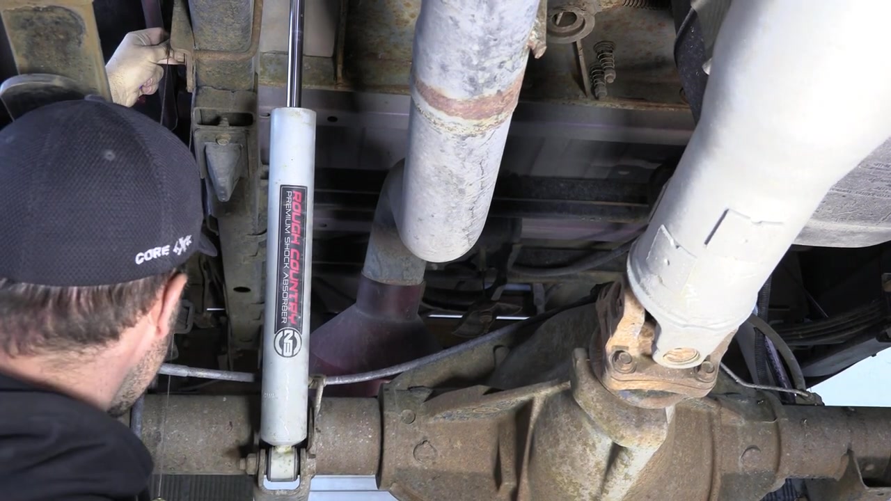 Close-up underneath the Ram 3500 rear axle showing the shock mount and suspension components before bracket installation