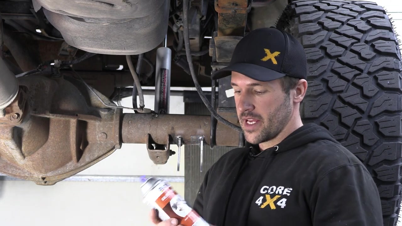 Spence holding the Dupli-Color Rust Barrier spray can with the Ram 3500 rear axle and freshly welded trailing arm brackets visible behind him