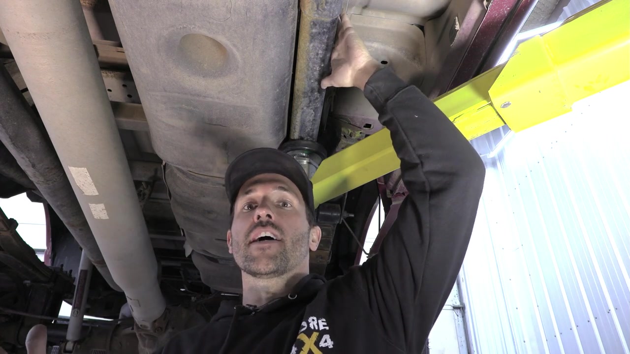 Spence working under the Ram 3500 near the fuel tank area on the driver side, using a transmission jack to lower the tank for frame bracket access