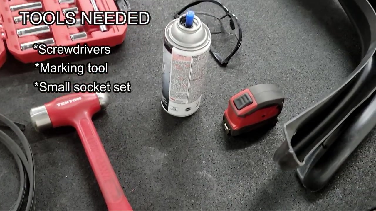 Tools needed for the rear fender flare install laid out on a workbench including screwdrivers, marking tool, socket set, hammer, tape measure, safety glasses, rattle can, and drill bits