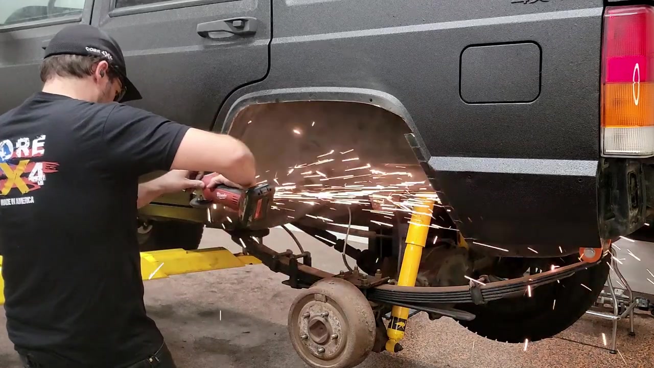 Spence using an angle grinder with a cut-off wheel to trim the rear fender of the Jeep XJ Cherokee with sparks flying