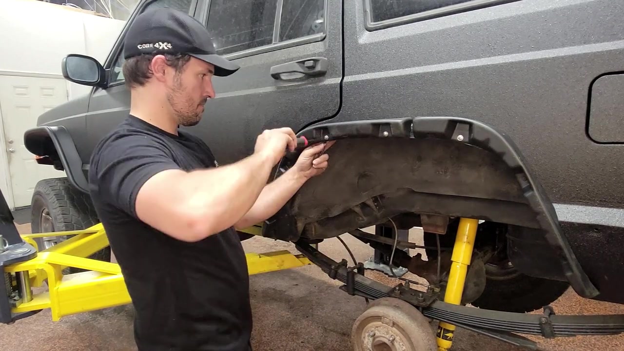 Spence bolting the rear fender flare support bracket onto the XJ Cherokee with the fender trimmed and folded