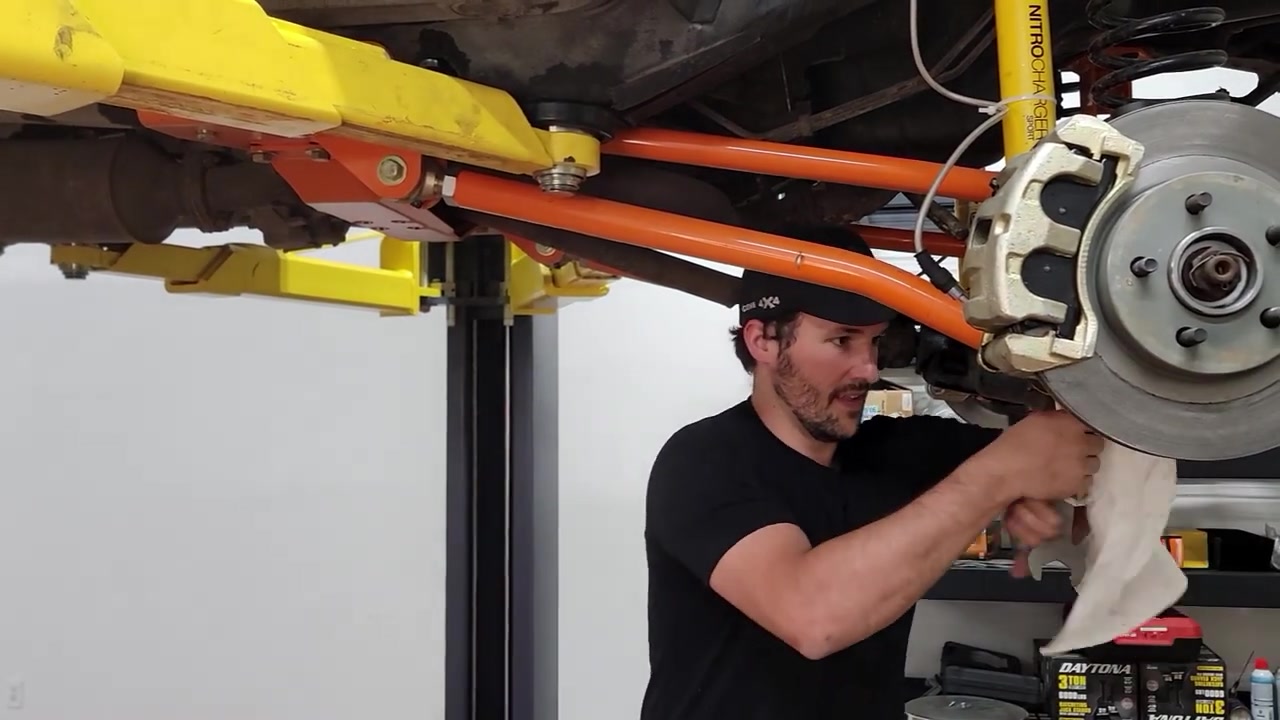Spence working under the XJ Cherokee on the lift, orange Core 4x4 long arms and front axle visible