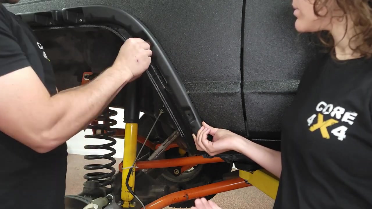Spence and Marissa positioning the fender flare support bracket inside the XJ wheel well to mark trim lines on the fender