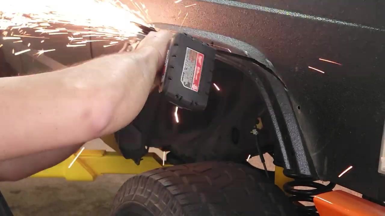 Using an angle grinder with sparks flying to smooth the cut edges of the XJ Cherokee fender opening with the fender support bracket visible