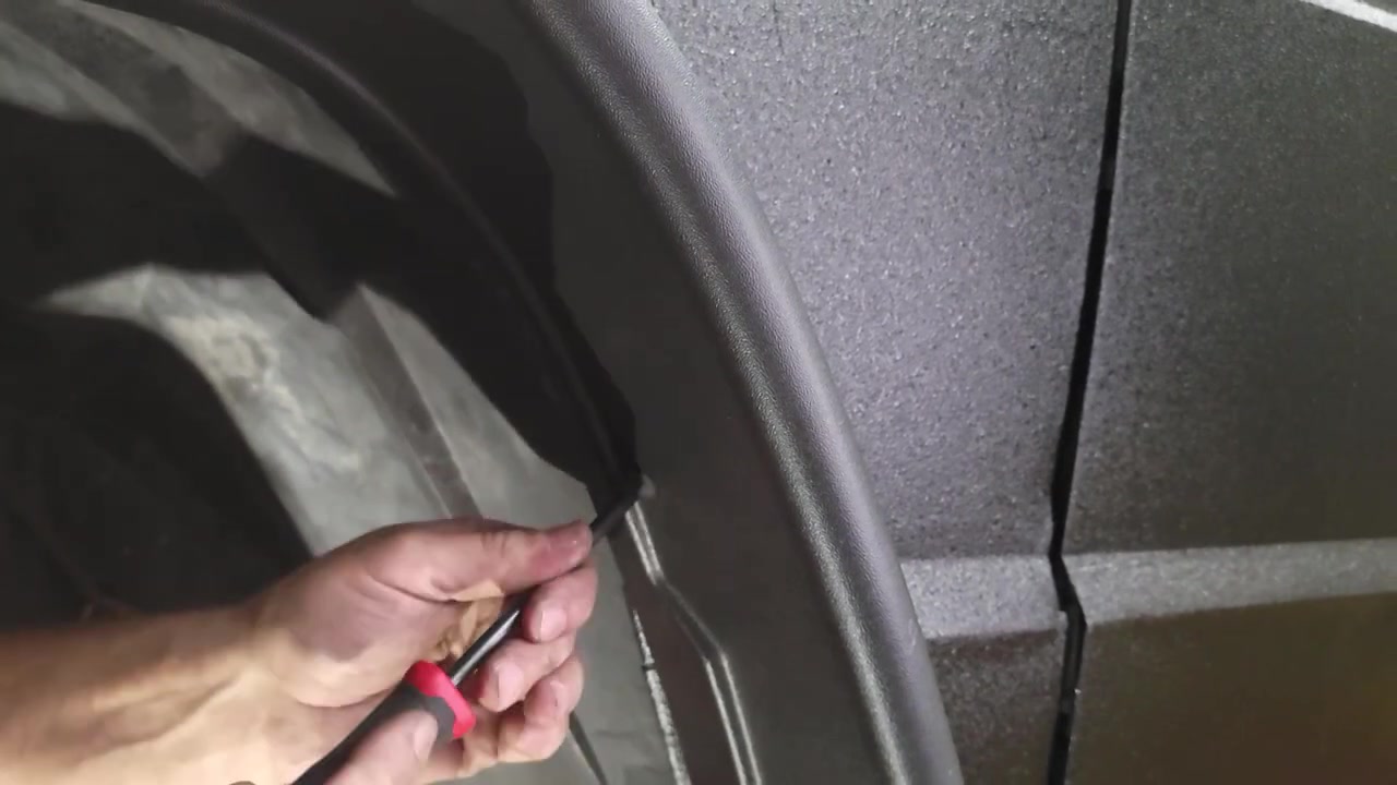Using a pick tool to align the fender flare mounting holes with the nut tabs on the XJ Cherokee during the final install step