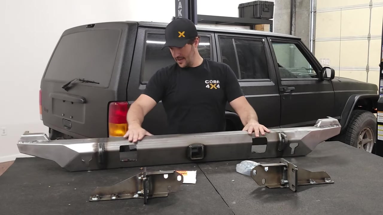 Spence examining the raw steel Dirtbound Highline rear bumper and brackets on the shop table with the XJ Cherokee in the background