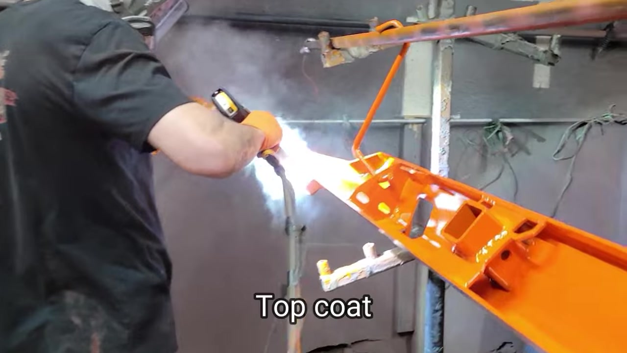 Applying orange powder coat top coat to the Dirtbound rear bumper bracket in the Core 4x4 powder coating booth