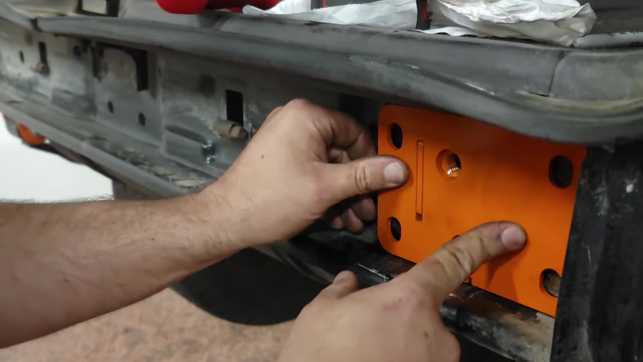 Orange powder-coated Dirtbound frame bracket being positioned inside the XJ Cherokee frame rail during installation