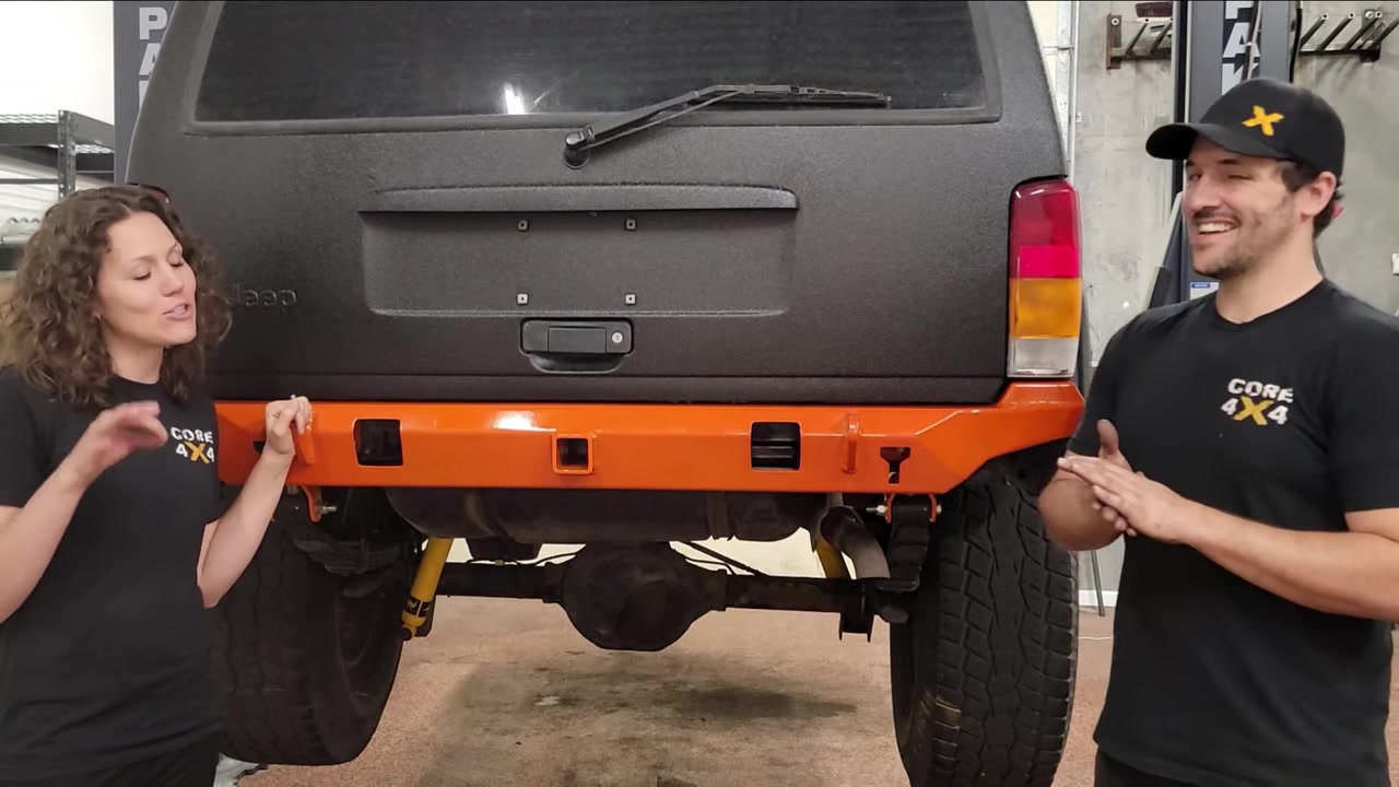 Spence and Marissa showing the finished orange powder-coated Dirtbound Highline rear bumper installed on the XJ Cherokee