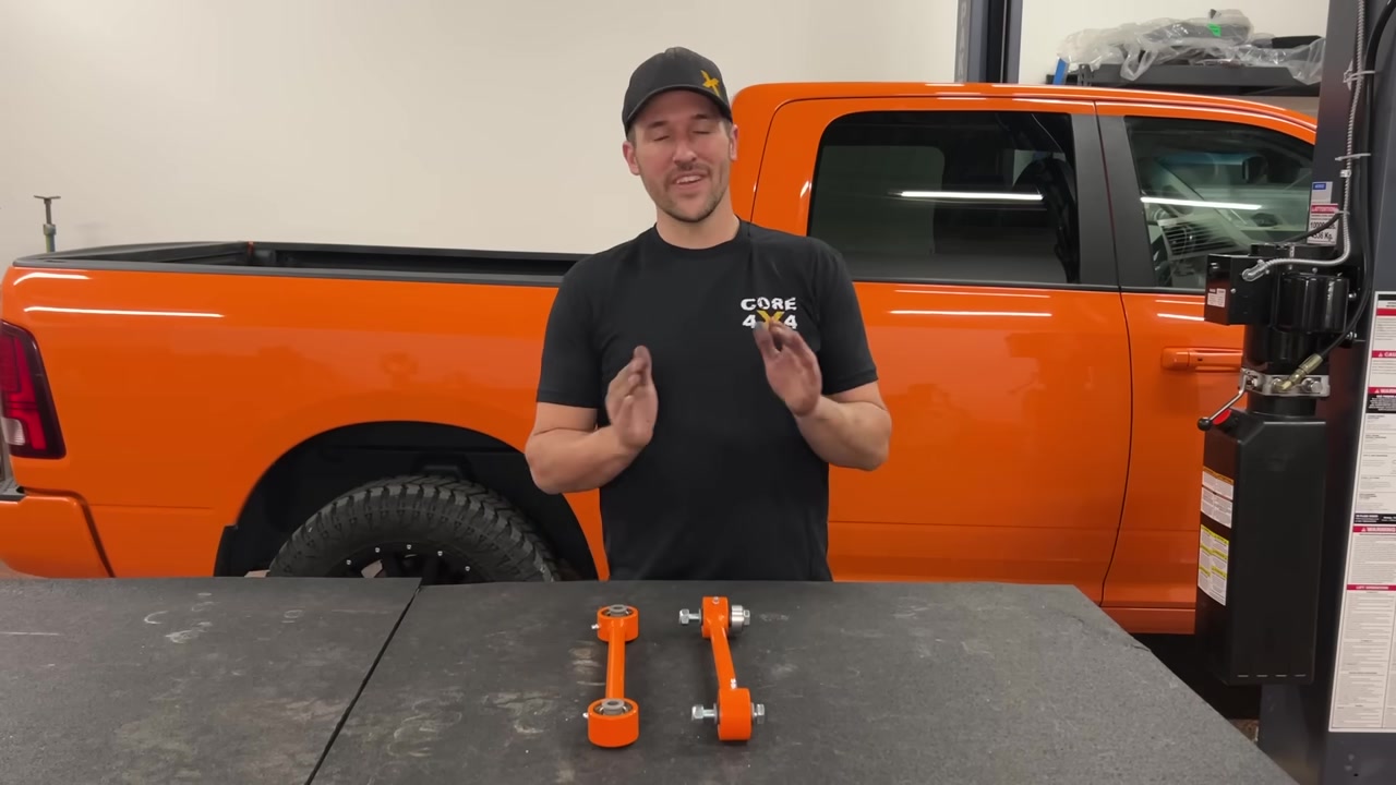 Spence from Core 4x4 standing behind the orange Ram 1500 in the shop with a pair of orange Core 4x4 Track Series sway bar end links on the table