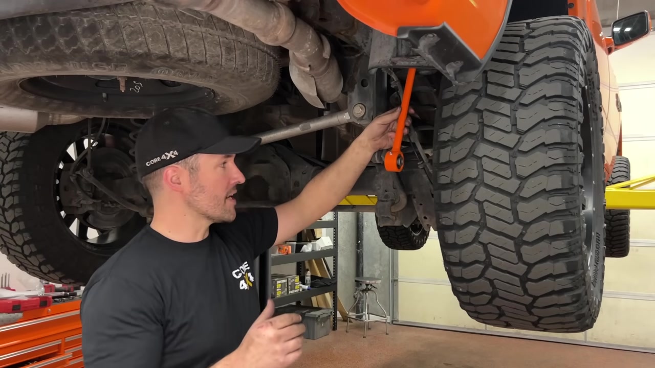 Underneath the orange Ram 1500 showing the rear sway bar area and factory end link before removal