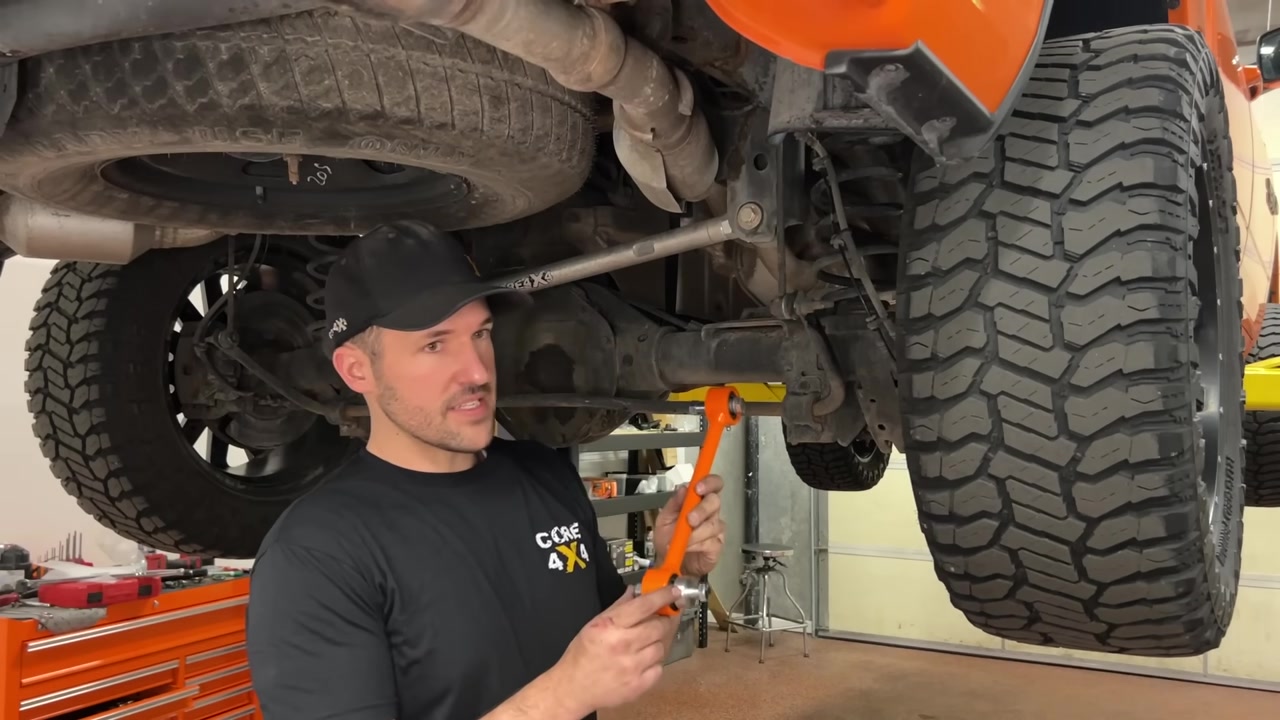 Spence holding a Core 4x4 orange end link next to the Ram 1500 rear sway bar mount showing the size difference versus factory