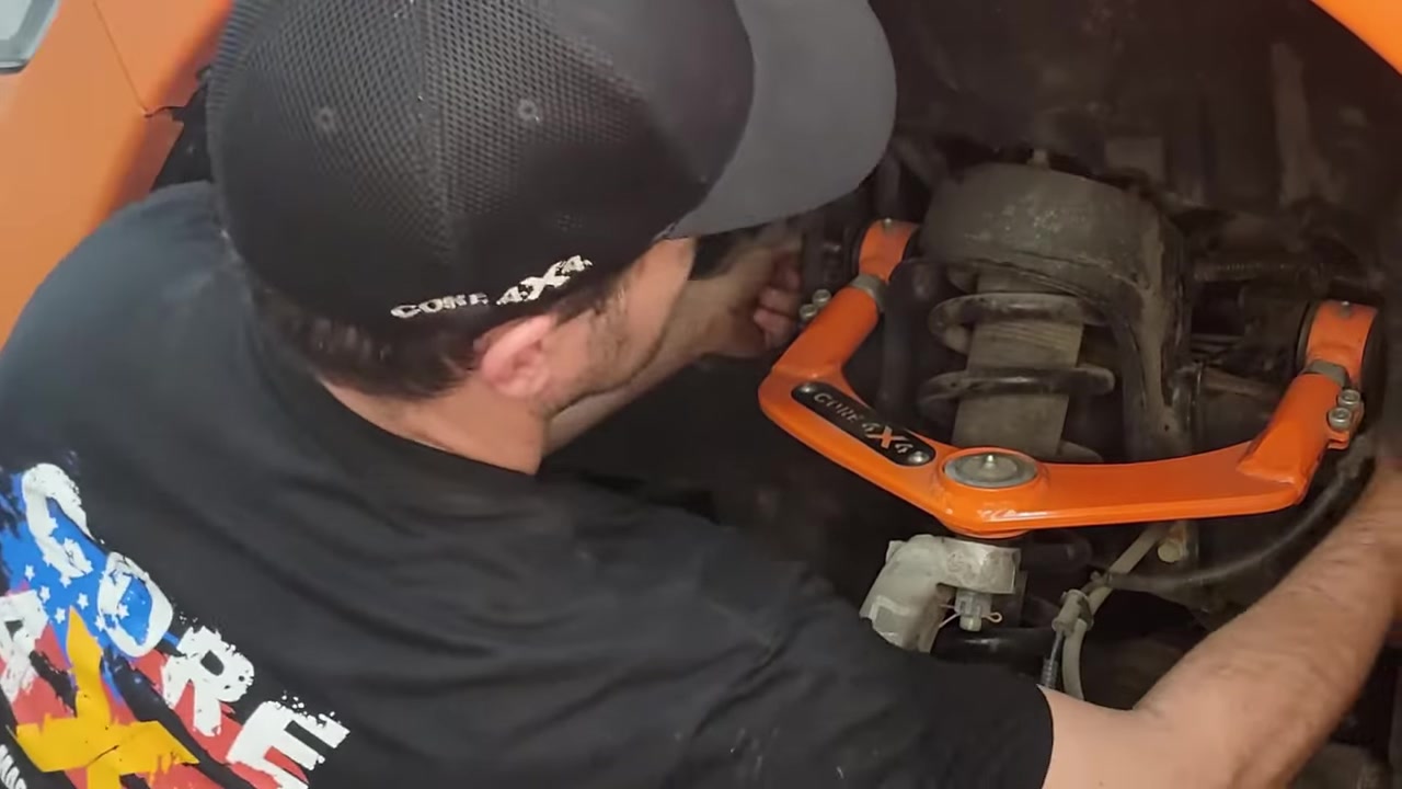 Spence installing the new Core 4x4 upper control arm into the Ram 1500 front suspension, showing the arm seated in the frame bracket with the ball joint entering the knuckle
