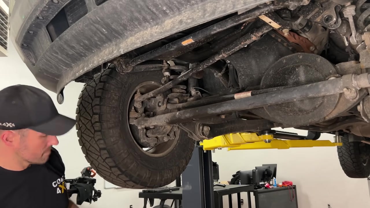Spence underneath the Ram 2500 showing the factory front track bar and axle mounting location