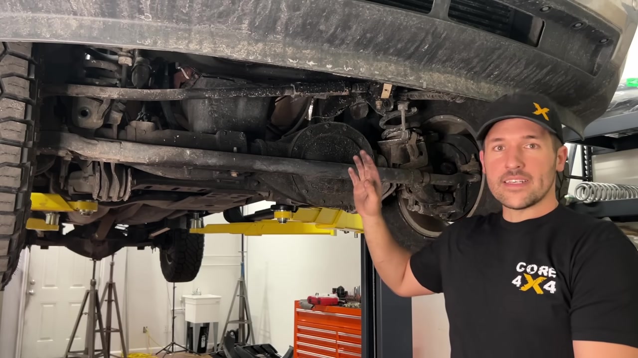 Spence under the Ram 2500 pointing at the factory track bar mounting area with the axle shifted after bar removal
