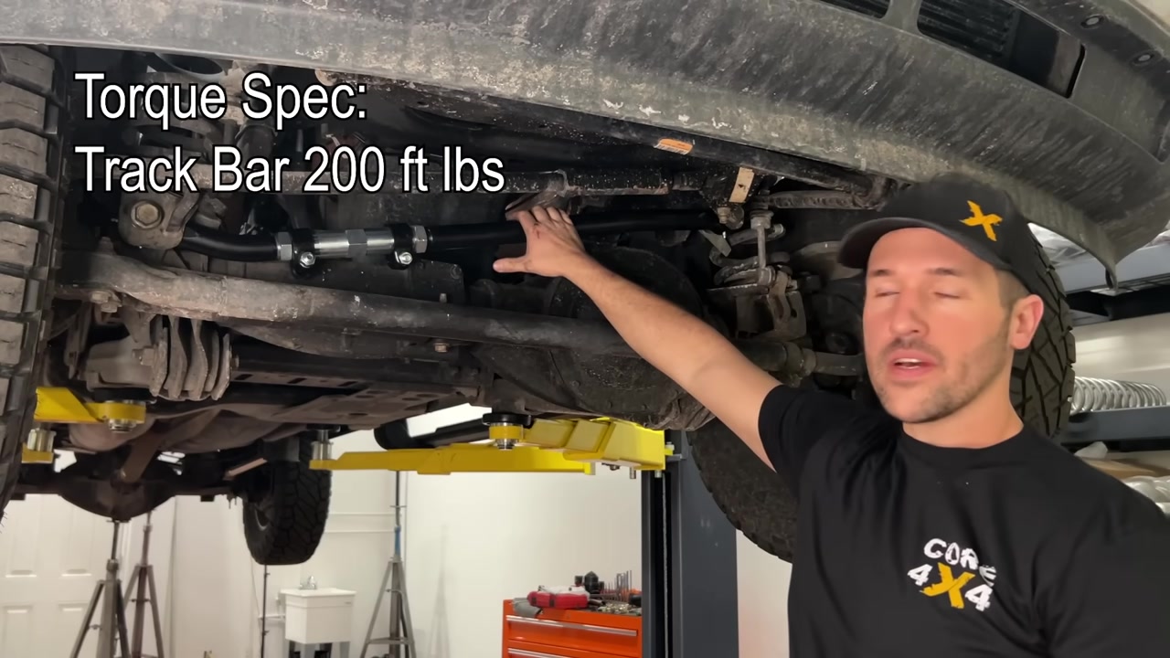 Spence under the Ram 2500 showing torque specs on screen: track bar bolts 200 ft-lbs, with the new track bar installed on the axle