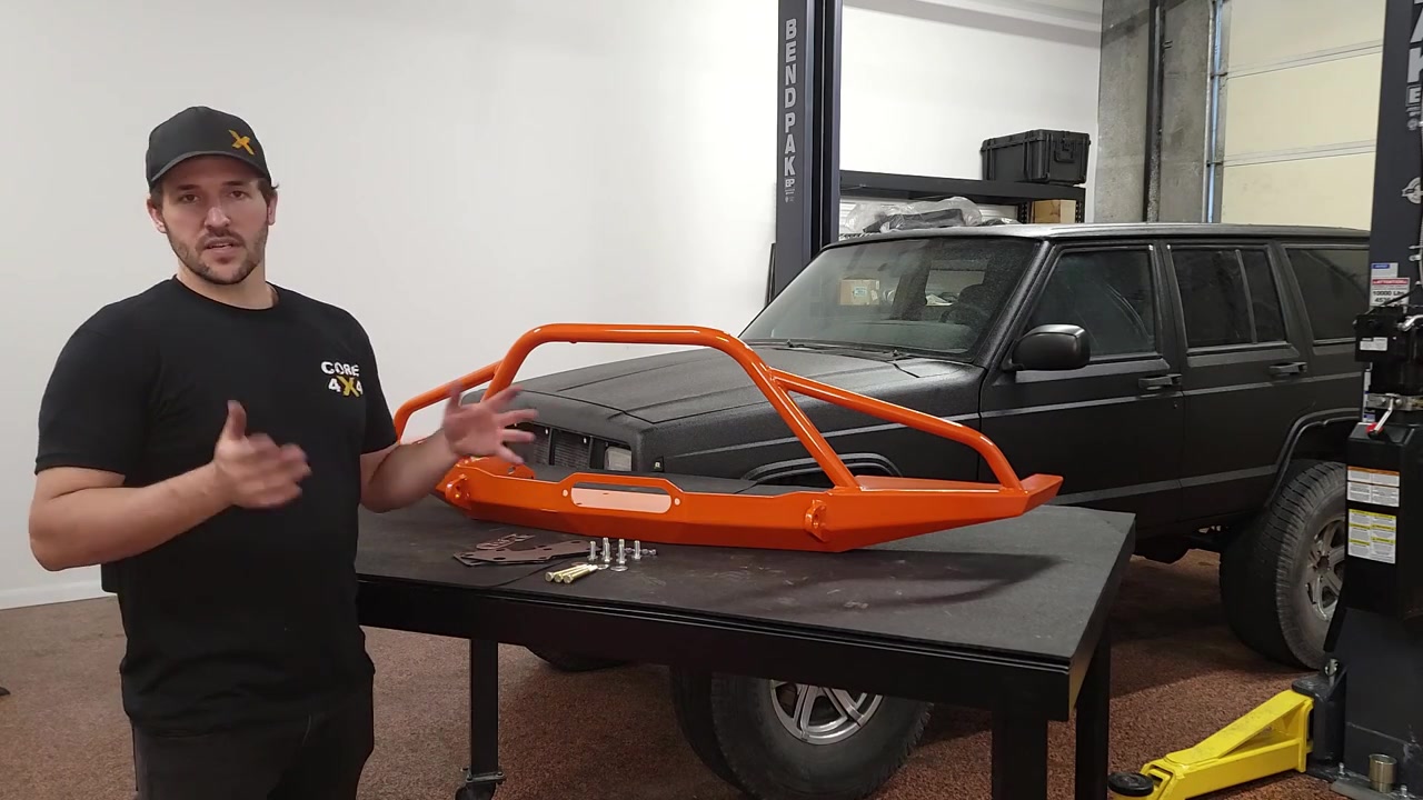 Spence presenting the powder-coated Dirtbound front bumper and frame brace hardware on a table next to the XJ Cherokee